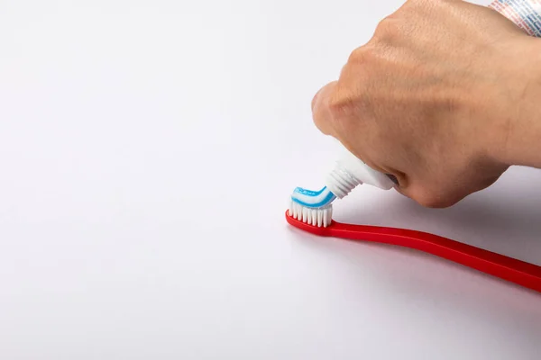 Putting toothpaste on red toothbrush. White background with space for text and information — Stock Photo, Image