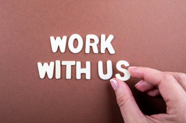 Bizimle çalış. Beyaz harfler ve kahverengi arka planda bir kadın eli.