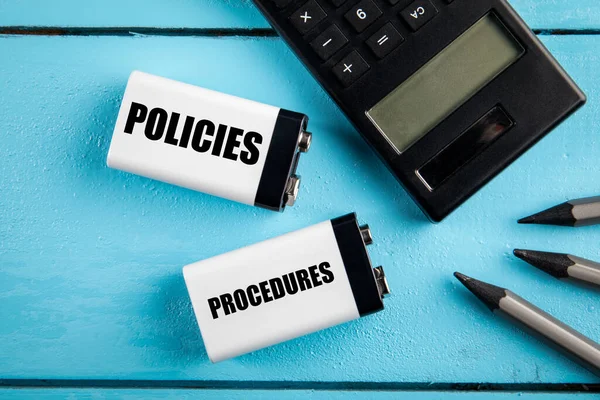 Concetto di politiche e procedure. Due batterie, una calcolatrice e una matita su uno sfondo di legno — Foto Stock