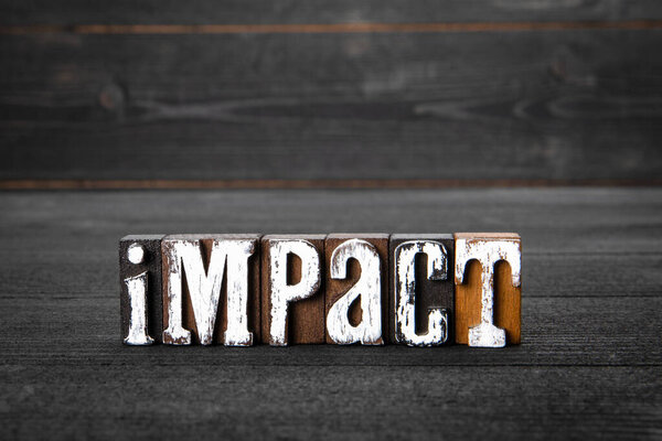 Impact. White wooden letters on a dark wooden background.