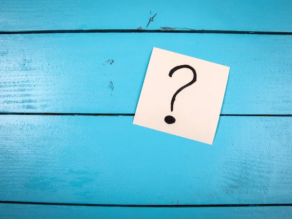 Uma nota branca com um ponto de interrogação em um fundo de madeira azul — Fotografia de Stock