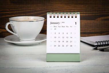 Ocak 2022. Masa takvimi, kahve fincanı ve ofis malzemeleri masanın üstünde.