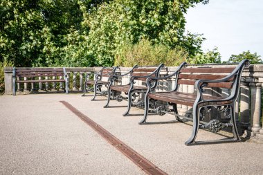 Süslü, siyah demir çerçeveli bir sıra klasik ahşap banklar sessiz bir parktaki yeşilliğe tepeden bakan bir taş korkuluğun yanında dururlar. Rahatlama, rahatlama ve sakin bir kamusal alan için