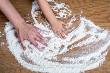 Yetişkin ve Çocuk Elleri Ahşap Mutfak yüzeyine un yayıyor.