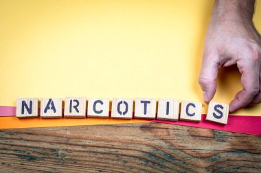 NARCOTICS kavramı, yasadışı uyuşturucu ticaretini gösteren elle düzenlenmiş ahşap harf bloklarıyla gösterilmiştir