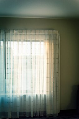 Beyaz perdeli bir otel odası, perdeli bir baton ve ışıklandırmalı bir sabah ışığı.