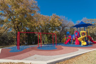 Sonbaharda halk parkının yanındaki kırmızı salıncakta çiçek tohumu, Teksas, Amerika 'da sonbahar yeşillikleri var. Döşemede kurumuş yapraklar var..