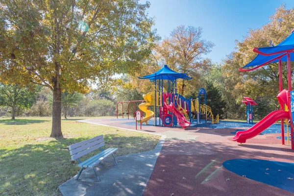 Colorful public playground near nature park with colorful fall foliage in Flower Mound, Texas, America. Kids recreation equipment with shade sail and red fire department theme