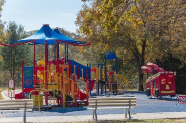 Arkadaki iki boş bankta sonbahar yaprakları ile renklendirilmiş oyun parkına bakıyor. Teksas, ABD