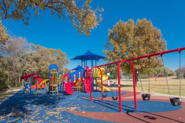 Doğa parkının yanındaki oyun parkında kırmızı salıncaklar ve renkli sonbahar yaprakları Texas, Flower Mound 'da.