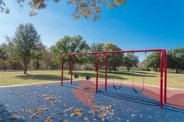 Close-up red swings in playground near nature park with colorful autumn leaves in Flower Mound, Texas, USA — Stock Photo, Image