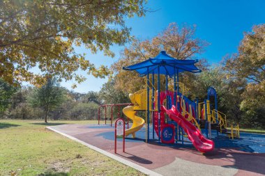 Doğa parkının yanındaki renkli halk parkı. Flower Mound, Teksas, Amerika 'da renkli sonbahar yeşillikleri var. Gölge yelkenli ve kırmızı itfaiye temalı çocuk eğlence ekipmanları.