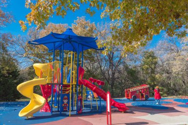 Doğa parkının yanındaki renkli halk parkı. Flower Mound, Teksas, Amerika 'da renkli sonbahar yeşillikleri var. Gölge yelkenli ve kırmızı itfaiye temalı çocuk eğlence ekipmanları.
