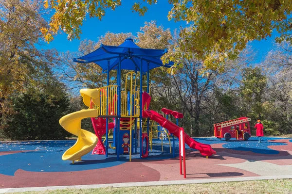 Colorful public playground near nature park with colorful fall foliage in Flower Mound, Texas, America. Kids recreation equipment with shade sail and red fire department theme