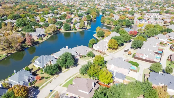 Top view upscale waterfront houses surrounded by colorful fall foliage in Coppell, Texas, America. Aerial view neighborhood lake with small dam and water fountain