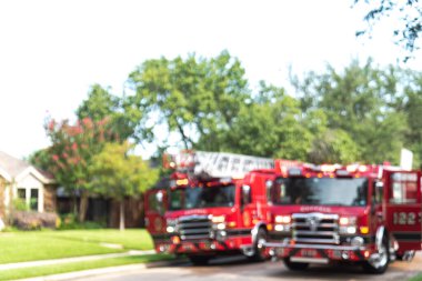 Bulanık soyut görüntülü itfaiye arabaları. Üzerinde parlayan ışıklar var. Dallas, Teksas, Amerika yakınlarında olgunlaşmış ağaçlar var. Banliyödeki yangın musluğundan su dökülmüş..