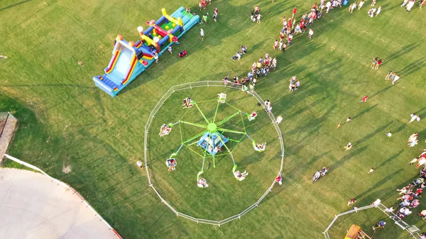 巨大な屋外カルーセルとカラフルなインフレータブルスライドで 子供たちは米国テキサス州フラワーマウントの公共イベントに乗っています パーティーや家族の活動に参加する人々の空中ビュー群衆 — ストック写真
