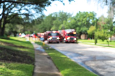 Bulanık soyut görüntülü itfaiye arabaları. Üzerinde parlayan ışıklar var. Dallas, Teksas, Amerika yakınlarında olgunlaşmış ağaçlar var. Banliyödeki yangın musluğundan su dökülmüş..