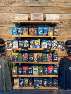 NORTH RICHLAND HILLS, TX, US-OCT 4, 25: Stacked coffee bags AK-47, Freedom Fuel, folded hoodies, hanging shirts displayed on wooden shelves in a rugged, organized layout at Black Rifle Coffee Company