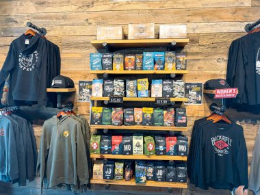 NORTH RICHLAND HILLS, TX, US-OCT 4, 25: Stacked coffee bags AK-47, Freedom Fuel, folded hoodies, hanging shirts displayed on wooden shelves in a rugged, organized layout at Black Rifle Coffee Company