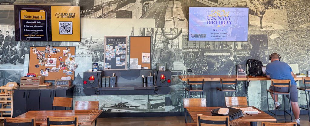 NORTH RICHLAND HILLS, TX, US-OCT 4, 25: Panorama view Black Rifle Coffee Company Cafe customer using laptop at high bar, military, red rotary phones, bulletin board, celebrating Army 250 birthday