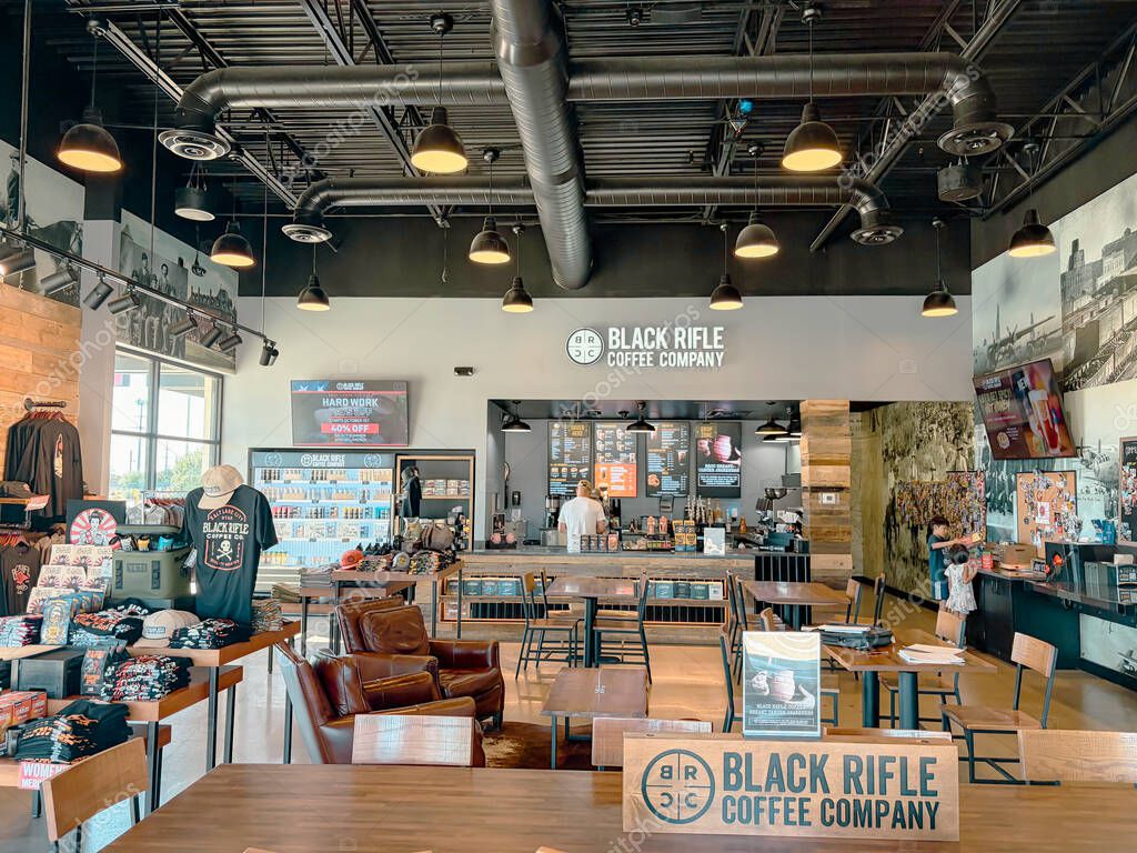 NORTH RICHLAND HILLS, TX, US-OCT 4, 25: Table surface logo Black Rifle Coffee with customers ordering drinks and children playing nearby, set against industrial ceiling pipes and warm wood furnishings