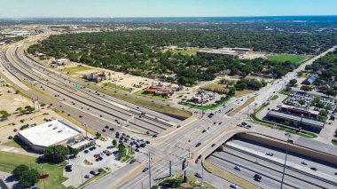 Curved NE Loop 820 highway interchange in North Richland Hills, Texas, intersecting restaurant pads, suburban homes, and school district stadium with green fields and layered zoning transitions. USA