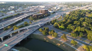 Lush urban park and tree canopy border the Trinity River, stacked highway ramps curving toward Fort Worth high-rise office buildings. Flyover blends mobility, green space, architectural density