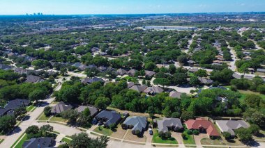 Large suburban subdivision of North Richland Hills, Texas with row of two-story houses, mid-ground industrial zone with warehouses and highway, distant Fort Worth skyline anchoring the horizon. USA