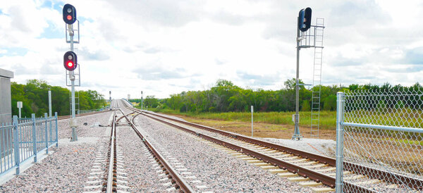 Комплексный железнодорожный узел с видом на Панораму рядом с аэропортом DFW показывает, что несколько путей расходятся, сближаются, красный сигнальный свет останавливает движение поезда. Гравийный балласт и ограждение укрепляют протоколы безопасности. США