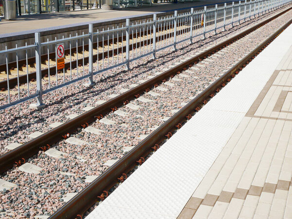 Крупный план чистая платформа для пассажиров, находящихся на борту возле станции DFW Airport. Бетонные плитки, тактильные полосы, прилегающие рельсы с гравийным балластом отражают пригородную готовность. США