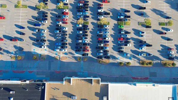 Değişik çatı kaplamaları olan alışveriş merkezinin dikey drone görüntüsü, çatı katı yoğunluğu, yoğun park alanı. ADA engelli alanları önceliği ve araç karışımı perakende erişilebilirliği ve imar stratejisini yansıtır. ABD