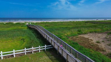 Çit ve merkez sahil yolu ziyaretçileri otlak kum tepelerinden Galveston beyaz kumlu plajlarına, sakin Körfez dalgalarına, açık gökyüzü altındaki uzak gemilere, kıyı erişimini ve ritmini vurgulamaya yönlendiriyor. ABD