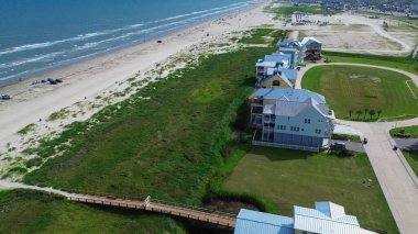 Dairesel garaj yolları ve metal çatıları olan yeni yapılmış yazlık evler South Beach, Galveston, TX yakınlarındaki kıyı şeridi, uzun beyaz kumlu sahil şeridi, geniş açık hava parkı ve çimenli boş arazi. ABD