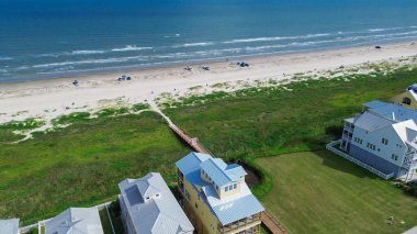 Yeni gelişim alanlarının yakınındaki boş alanlar pastel kaplamalı ve metal çatılı evler, Galveston 'a giden tahta kaldırımlar, plaj aktiviteli TX kumlu sahil şeridi, park edilmiş arabalar ve çöp tenekeleri. ABD