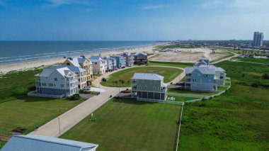 Garaj yolları ve balkonları olan durgun yazlık evlerden görülebilen ıssız bir apartman dairesi, South Beach, Galveston, Texas yakınlarındaki çimenli arazinin yanında duruyor, uzun beyaz kumlu sahil şeridi, sakin dalgalar. ABD