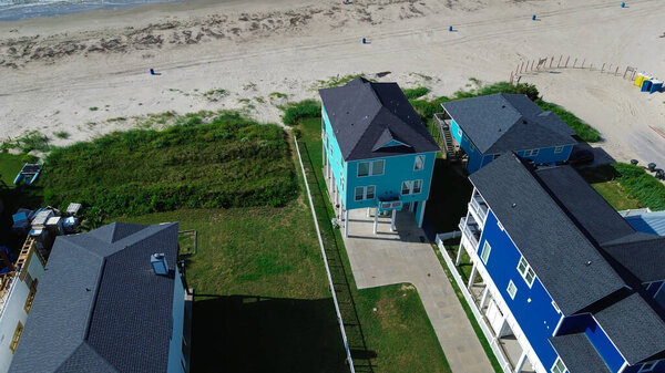 Вход на пляж в Бичсайд-Виллидж, Галвестон, штат Техас, имеет барьер, ведущий к белому песчаному побережью, граничащему с жилыми домами с балконами, пальмами и видом на океан. США