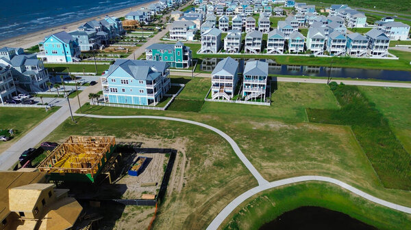 Смешанная фаза строительства вблизи Солнечного берега, Галвестон показывает в рамке, окутанные ходулями дома рядом с готовыми объектами. Постоянное расширение, архитектурная согласованность в зонах, подверженных наводнениям, мастер-планирование. США