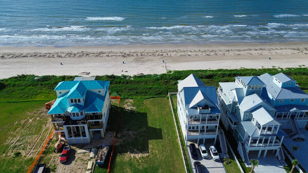 Прибрежные дома на сваях возле Солнечного берега, Галвестон, штат Техас, показывают дом с голубой крышей в середине строительства рядом с завершенными прибрежными жилыми домами. Высокий дизайн отражает устойчивое к наводнениям планирование. США
