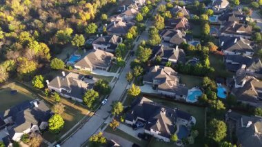 Lantana, Teksas 'ta ağaçlarla kaplı bir banliyö caddesinde, geniş eğimli planlar, lüks tuğlalı malikaneler, manzaralı bahçeler, sonbahar yaprakları, sık orman kenarındaki yeşil tamponların yanında yuva yapmış arka bahçe havuzları.