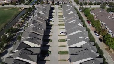 Aynı iki katlı evler, hafif tuğlalar ve yan yatmalar ortak bir garaj yolunda karşı karşıya. Yaya köprüsüne sahip kanal, yeşil alan yoğun yerleşim alanına zıtlık ekler, Çiçek Tepesi, Teksas