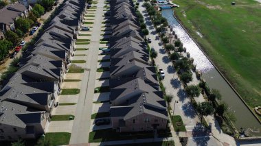 Çimenli boş arazi ve kanallar, yakın mesafeli banliyö evleri, üniformalı çatılar ve küçük yeşil çimen bantları, Teksas 'ın Çiçek Dağı' nda uzun gölgeler bırakan park edilmiş araçların olduğu bir caddeye bakıyor. ABD