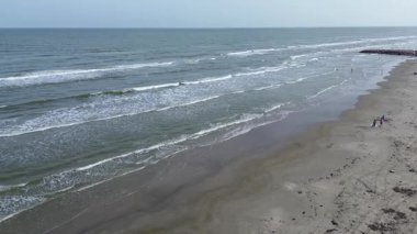 Kıvrımlı sahil şeridi, uzak iskele, birkaç kumsalcı ve yumuşak dalgaların Porretto Sahili, Galveston, Teksas yakınlarında kırıldığı sakin bir sahil manzarası.