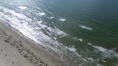 Çapraz kıyı şeridi Stewart Yolu, Galveston, TX güneş ışığını yansıtan koyu yeşil su, kumlu plaj yamaları, görünür deniz yosunu ve körfez manzarasından keyif alan dağınık ziyaretçiler, dinamik kıyı şeridi.