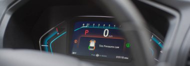 Panorama manzaralı araç park modunda, hız 0 mil. Turuncu göstergelerle birlikte lastik basıncı uyarısı aktif. Soğuk hava şartlarının düşüşünü, sürücü güvenlik risklerini, danışmanlık seçeneklerini, entegre yol kenarlarını vurgulamak. ABD