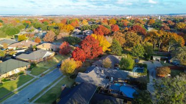Kırmızı, turuncu, sarı, canlı sonbahar yeşillikleriyle çerçevelenmiş düzgün düzenlenmiş evler. Garaj yolları, çatılar, arka bahçe havuzları organize banliyö duvar halılarına ritim katıyor. Coppell, Dallas, TX. ABD