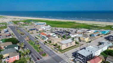 Hava görüntüsü ana yolu çapraz olarak Stewart Sahili 'ne doğru yerleşim ve ticari bloklar üzerinden kesiyor. Kırmızı çatılar, yeşil çimenler, kumlu dokular körfez kıyısında birleşiyor, Galveston, Teksas. ABD