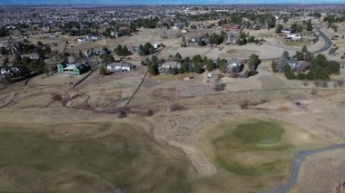 Saddle Rock Golf Kulübü 'nün doğu kıyısındaki dağınık evler kuru arazi ve seyrek ağaçların arasında otururlar. Kahverengi çimenler, kum sığınakları, uzak şehir silueti mevsimsel kontrastlar, Aurora, Colorado