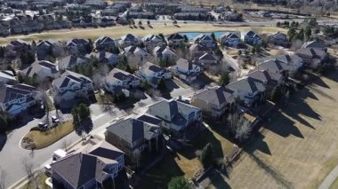 Doğu Calhoun Yolu yakınlarındaki yakın boşluklu evler küçük gölet etrafında kavis oluşturuyor ve çatıları ve yapraksız ağaçları olan parklar. Garaj yolları ve park halindeki araçlar kış düzenini noktaladı, Aurora, Colorado