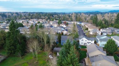 Meridian Gölü koridoru boyunca Doğu Tepesi 'ni Maple Vadisi' ne bağlayan yumuşak bir yükselti üzerinde oturuyorlar. Kiremit desenleri, garaj yolu çizgileri, yoğun yeşil dokular katmanlı görsel derinlik yaratır, Kent, WA. ABD